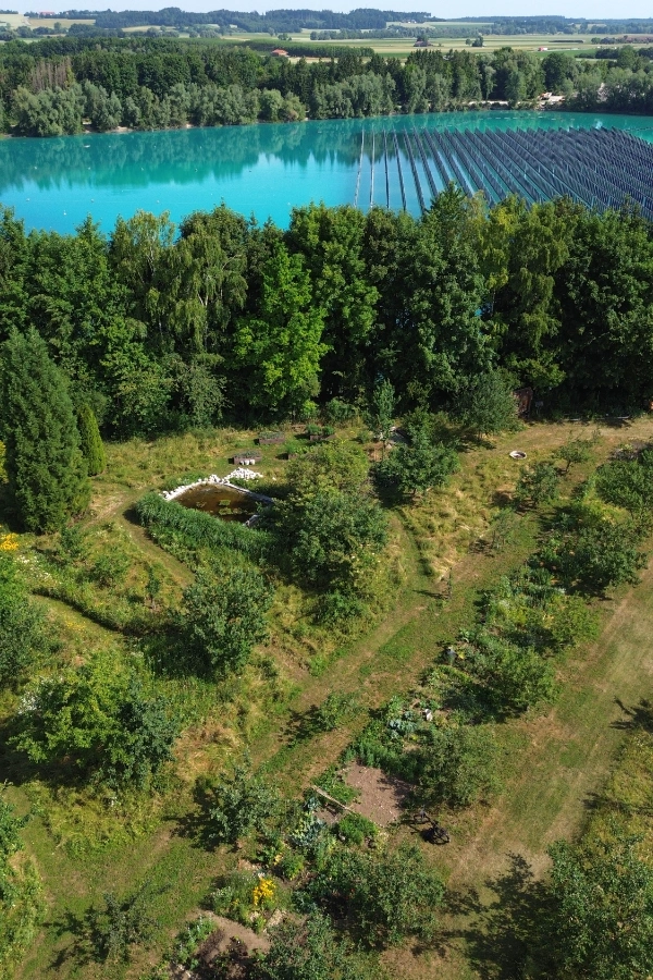Luftaufnahme des Lehrgarten Gilching im Vordergrund mit Blick auf schwimmende Photovoltaikanlage im Kieswerk Jais.